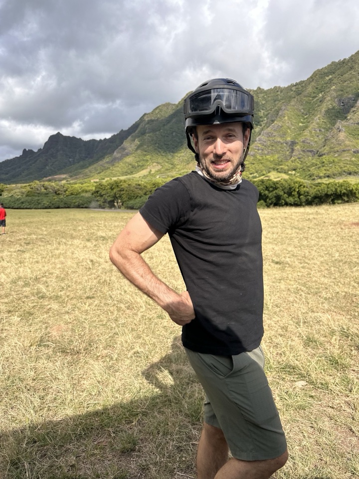 Russell Richardson in a helmet and black T-shirt in front of green mountains